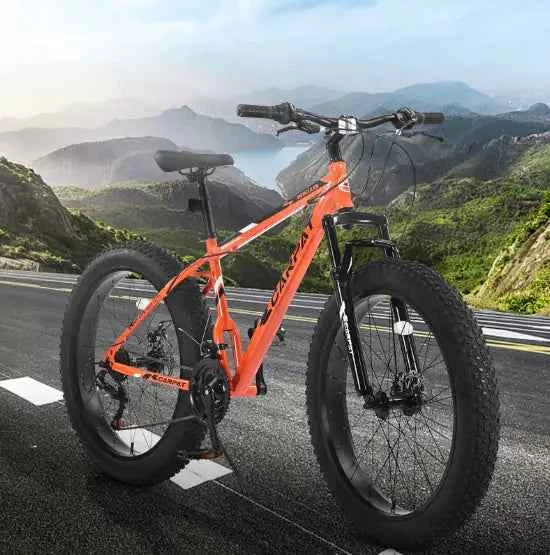 Orange mountain dirt bike with knobby tires on a paved mountain road with scenic hills in the background